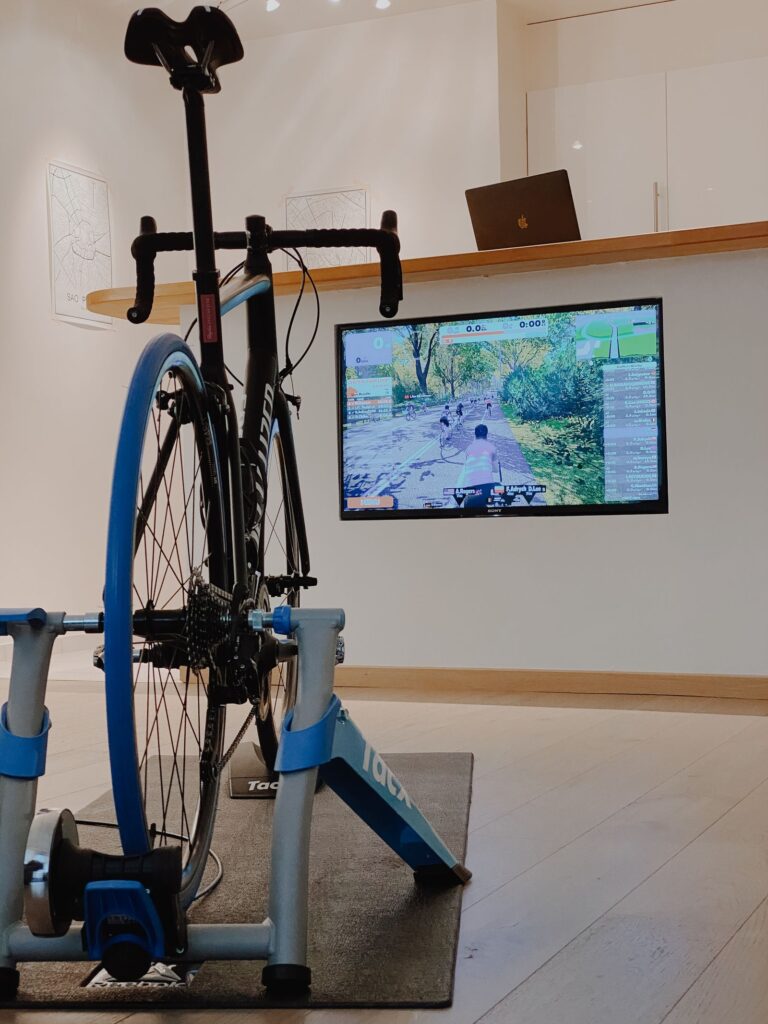 Racefiets op een smart fietstrainer in huis, met een virtuele fietsapp op het scherm